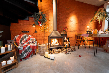 Naklejka premium Fireplace area of a beautiful loft-style interior with real brick and concrete floors decorated for the New Year holidays. The concept of home comfort