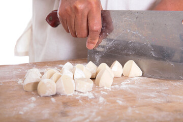 The pastry chef cuts the long white noodles into small dough with a kitchen knife