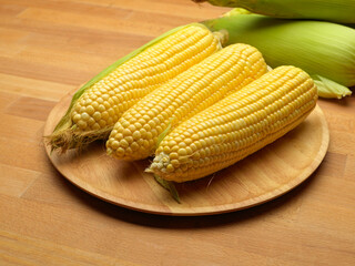 Close up view of corns and corn on the cop on wooden tray on wooden table with copy space