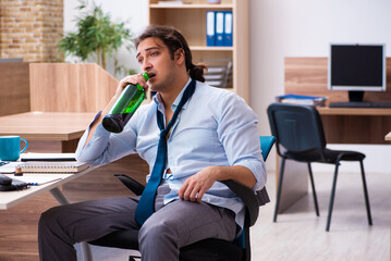 Young male employee drinking alcohol at workplace