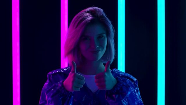 Portrait of a young stylish woman looking at the camera smiling and showing thumbs up gesture. Close up. Slow motion.