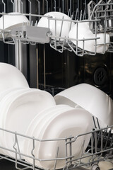 white plates and cups in the dishwasher compartment, close-up, side view