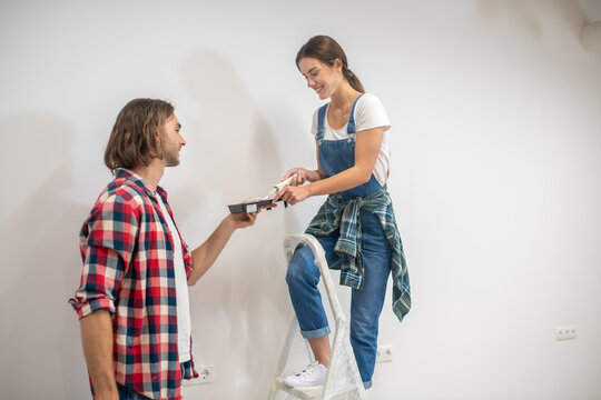 Young Woman Standing On Stepladder And Man Helping Her To Get Down