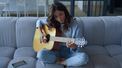 Focused girl learning to play guitar at home. Young woman playing guitar