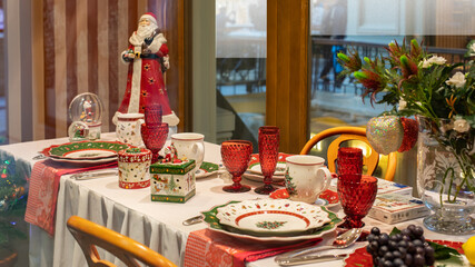 Festive Christmas decoration of the dinner table. Beautiful green red service, plate glass cup. Santa Claus in a red coat and a box with a gift