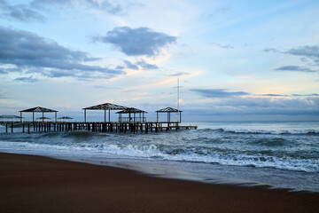 View from beach to water of sea, waves with white foam, pierce and sky with clouds in a nice evening.