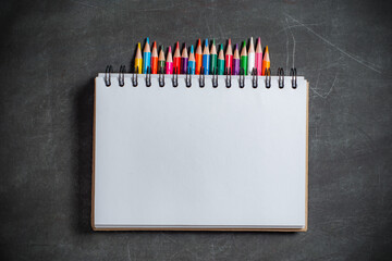 white notebook lies on a set of multi-colored pencils on a dark background