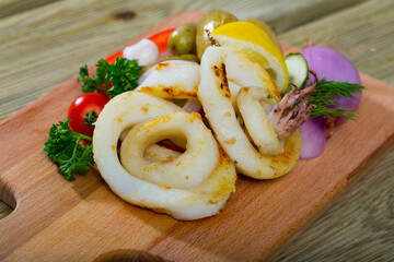 Healthy cuisine. Baked calamari rings served on wooden board with potatoes and fresh vegetables and greens