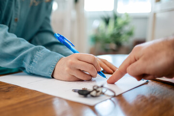 A realtor points to the contract for signing. Hands close-up. There are keys on the table. World leasing day. Side view