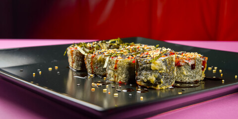 Sushi set served on a black square plate over bright pink background. Traditional Japanese cuisine, sushi rolls close up