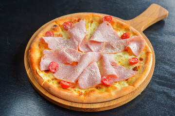 Pizza with bacon, salami and vegetables. Ham and tomatoes pizza with melted cheese.