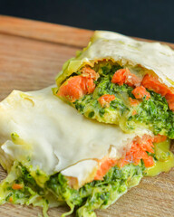 Wrap sandwich with pink salmon and spinach in lavash bread. Delicious snack concept, served on a rustic wooden board.