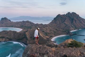 Young Asian man traveller holding camera and standing on top of Padar island in a morning sunrise, Komodo national park in Flores island, Indonesia