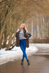 Beautiful blonde girl walks in the park in winter in a fur vest