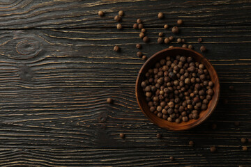 Bowl with peppercorns on wooden table, top view