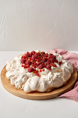 food, culinary, baking and cooking concept - close up of pavlova meringue cake decorated with red berries on wooden serving board and kitchen towel