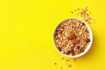 Bowl with granola with nuts and raisins on yellow background