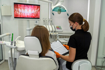 Obraz premium Professional dentist with clipboard talking or recording diagnosis with patient before treatment