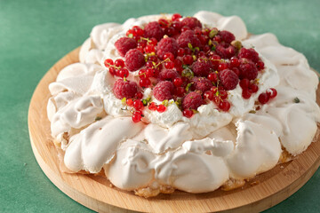 food, culinary, baking and cooking concept - close up of pavlova meringue cake decorated with red berries on wooden serving board