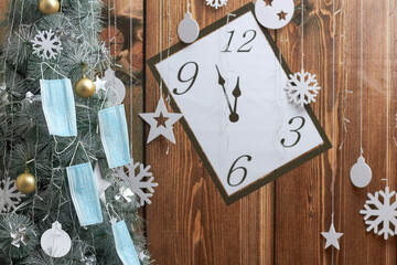face masks hang on a Christmas tree, on a wooden clock background. Pandemic.