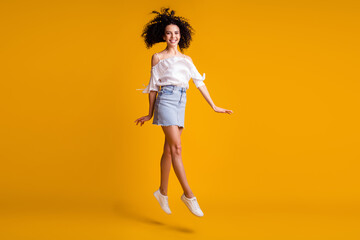 Fototapeta na wymiar Photo portrait of jumping high girl walking going wearing jeans mini skirt sneakers isolated on vibrant yellow color background