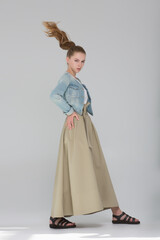 The model girl stands in a long skirt and blue jute. She takes a long stride, her hair in motion. Fashion look.