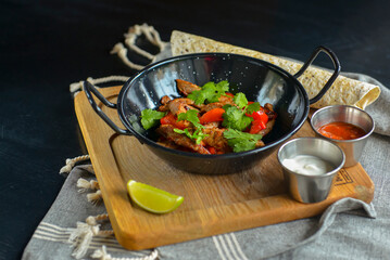 Vegetables and meat in wok pan served with lavash bread and different kinds of sauce. Close up.