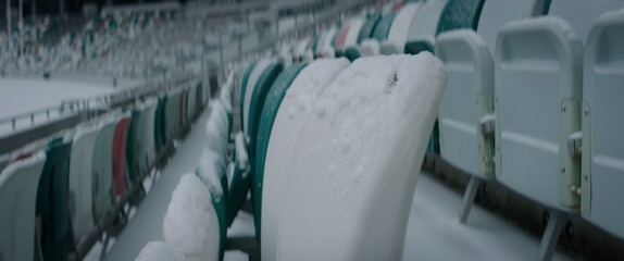 Fototapeta premium Empty outdoor football soccer stadium seats covered with snow in winter, light snowfall. Shot with 2x anamorphic lens