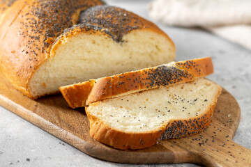 Homemade crusty loave of wheat candy bun with poppy seed on wooden background. Still life, dark mood, banner layout. Traditional techniques bakery concept