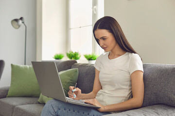 Woman reads information in a laptop and writes it in a notebook, drawing up a new business plan.