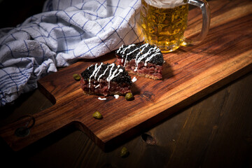 Gourmet Rindertatar Beef Tatar roh aus Filet fettarm, Kapern, Eigelb, Zwiebeln auf Toast Brot und schwarzer Kaviar, Schmand mit Bier, Küchentuch und Holzbrett Hintergrund dunkel