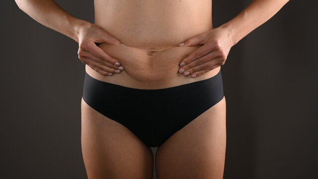 Woman in black panties squeezing fat at waist, close-up. Isolated on dark gray background