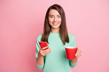 Portrait of attractive cheerful girl drinking tea using device gadget app isolated over pink pastel color background