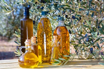 Poster Decanters and bottles with golden olive oil, fresh and pickled olives on wooden surface outdoors © JackF
