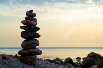 Pebble beach, beautiful view. Sun beams on sunrise and stones pyramid on the seashore. Rest and seaside vacation. Concept of balanced life, harmony and relax.