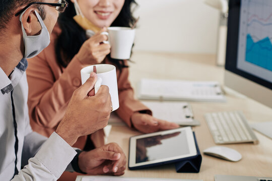 Cropped image of smiling business colleagues drinking coffee and discussing reports and charts at meeting in office