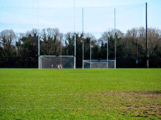 Green grass on a training field in focus, Two tall goal posts for Irish National sports camogie, hurling, rugby, gaelic football, soccer. warm sunny day, Nobody. Outdoor activity concept