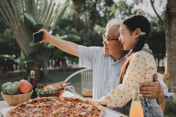 Grandfather and granddaughter having dinner in garden at home. Retirement age lifestyle with family...
