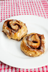 Hand made tasty cinnamon roll on a white plate and red and white table cloth. Pastry product.