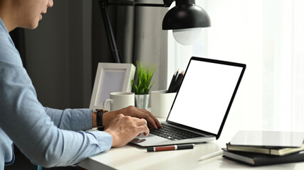 Side view of businessman working on laptop computer with blank screen at his workspace.