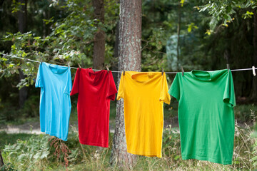 Four colorful t shirts hanging on a clothesline, drying out in the nature.
