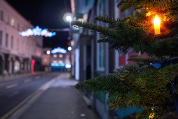 Night scene, candle on a fur tree in focus, town decorated and illuminated for Christmas out of focus. Festive season concept