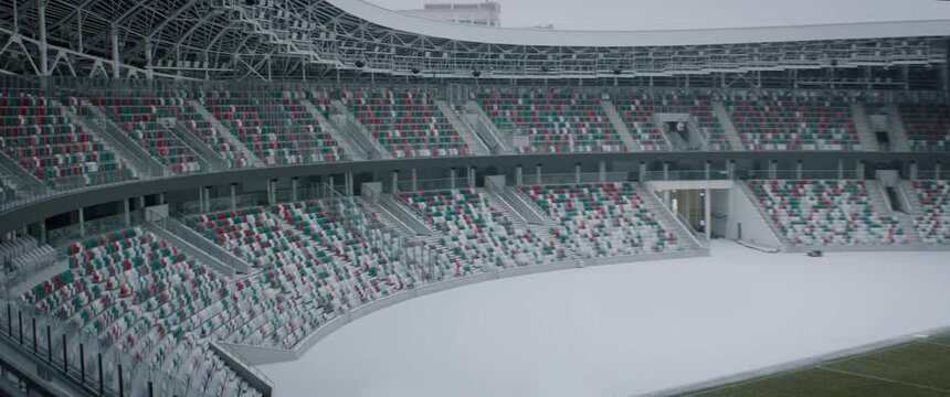 Empty outdoor football soccer stadium seats covered with snow in winter, light snowfall. Shot with 2x anamorphic lens. 120 FPS Slow motion