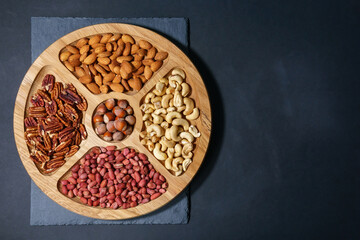 nuts in a wooden bowl on a dark table. Pecans, Cashews, hazelnuts, almonds, peanuts. Top view with space to copy.