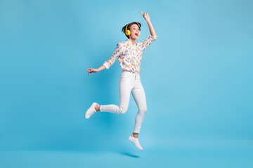 Fototapeta na wymiar Full size photo of young girl happy excited jump listen music earphones show finger empty space isolated over blue color background