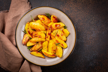 Oven roasted  potatoes with garlic, olive oil and rosemary. Vegan food. Top view, dark brown dark, brown,  background.