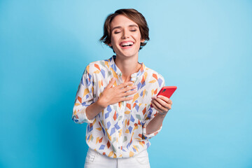 Photo of funky happy young woman closed eyes laugh hold phone wear white print shirt isolated on blue color background