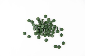 Green spirulina pills are scattered on a white background. Copy space.