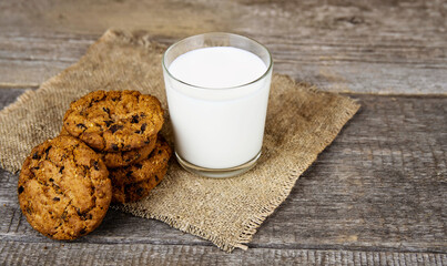 Glass with milk and oatmeal cookies on burlap on a wooden background.