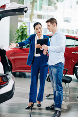 Car dealership manager showing big trunk of automobile to young customer